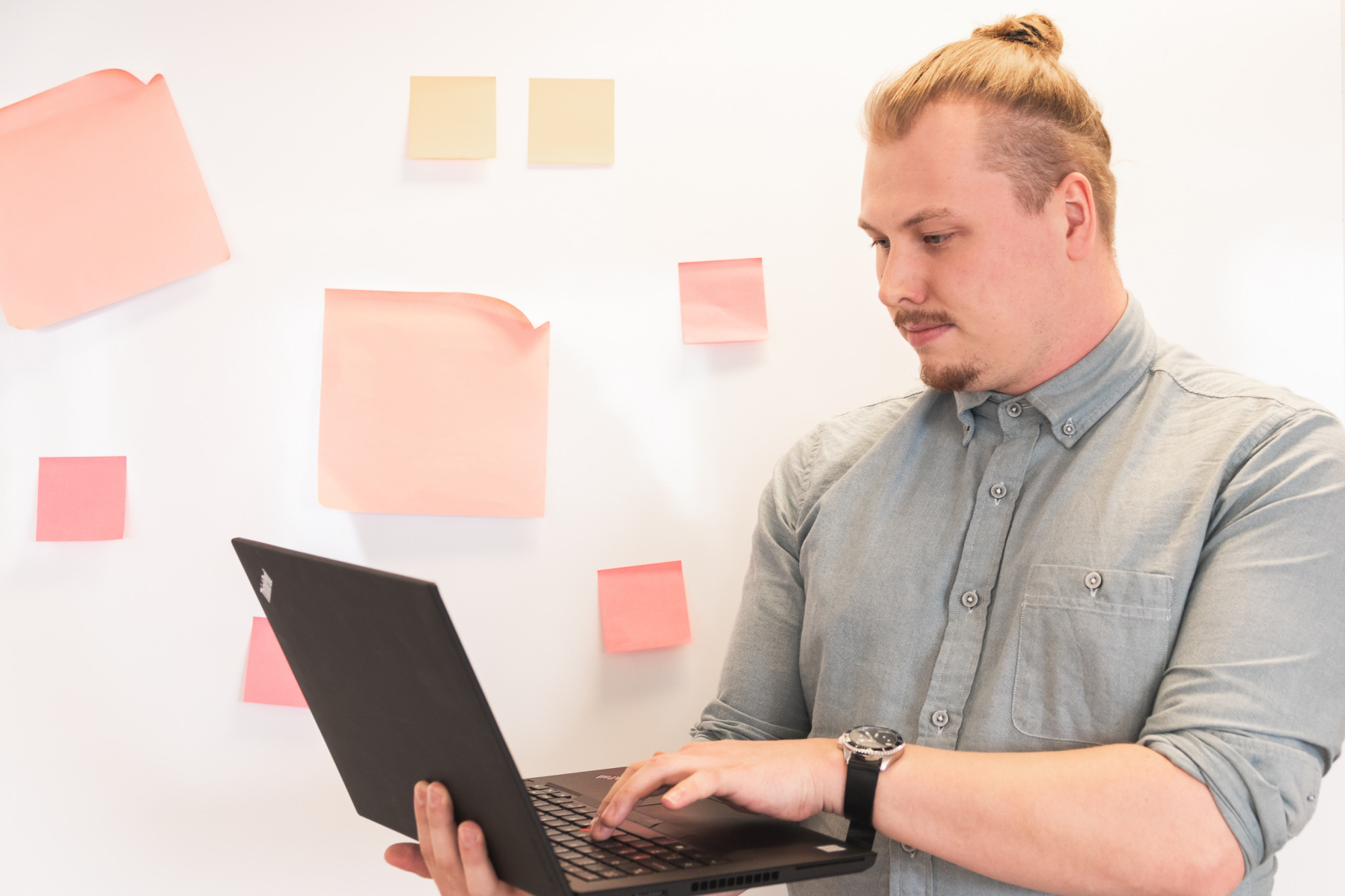 Henkilö tietokoneella valkotaulun edessä, jossa post it-lappuja.
